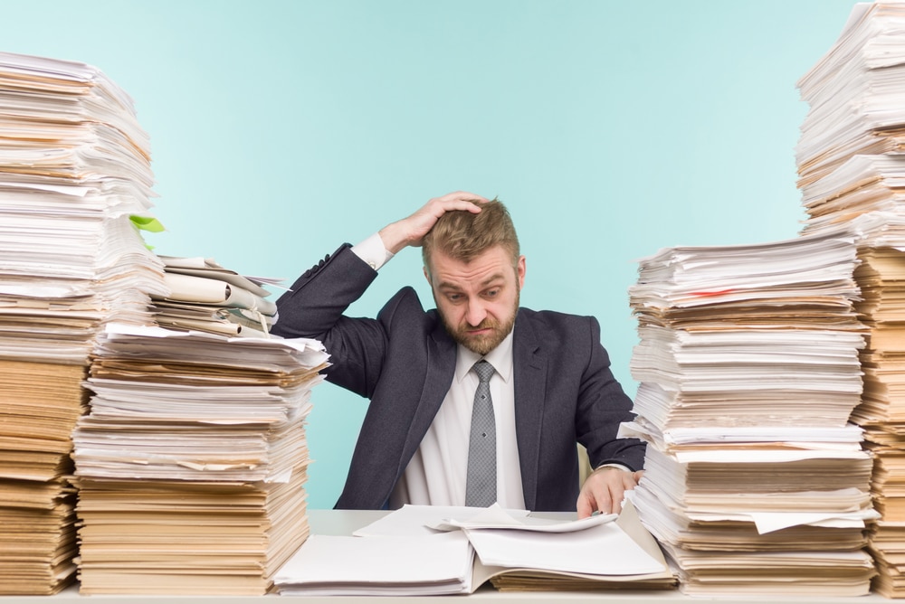 Frustrated-businessman-surrounded-by-stacks-of-paperwork