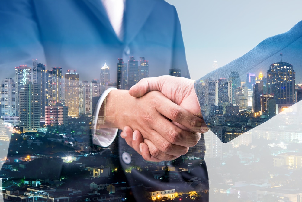 Two-businessmen-in-suits-shaking-hands-with-view-of-city-overlaid
