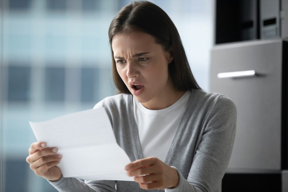 Woman-wearing-shocked-expression-while-looking-at-piece-of-paper